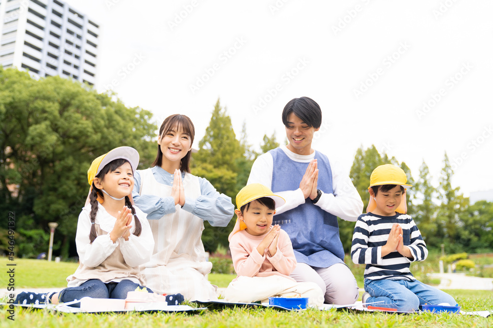 公園でお弁当を食べる保育士と園児