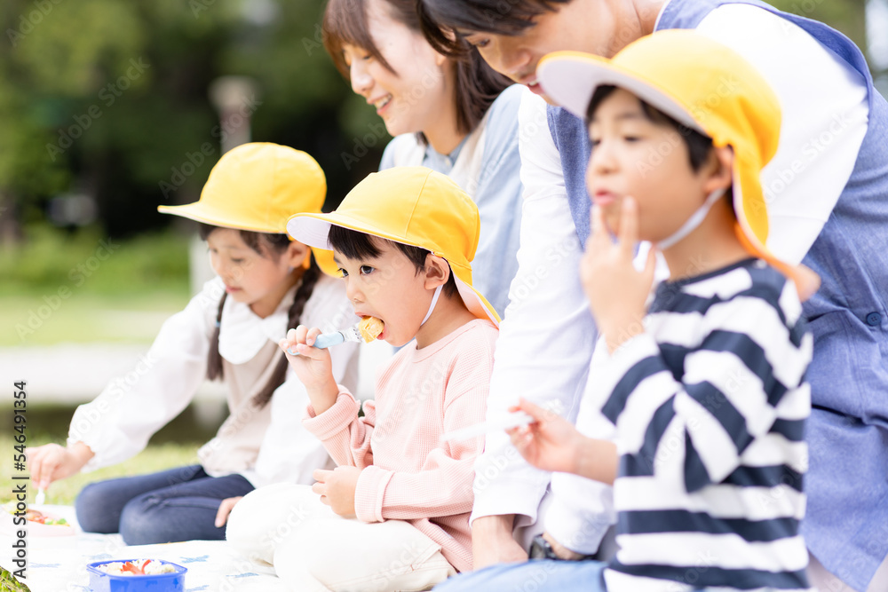 公園でお弁当を食べる保育士と園児
