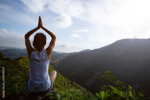 Yoga woman meditating on mountain peak cliff edge in the sunrise