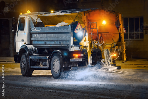 Truck spread salt and sand on snowy city road during blizzard at night shift, night work road maintenance. Snow and ice removing service. Salt spreading on snowy road, melt snow and ice. Deicing work photo