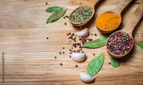 Spices and herbs for cooking. Spice greens in spoons on wooden background. Curry, turmeric, basil, pepper garlic and bay leaves.