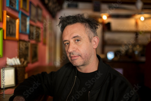 Portrait of a man looking at the camera. Image taken inside a colorful defocused cozy pub.