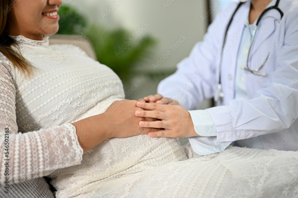 Asian pregnant woman is reassured by a professional female doctor, touching her belly.