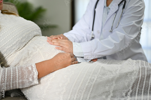 Female doctor or obstetrician checking up her patient, touching belly of her pregnant patient.