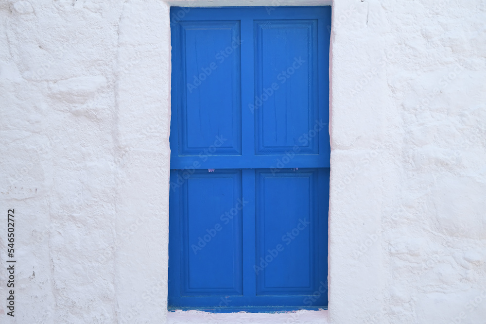 Bright blue door on white wall of historic building, window with closed shutters