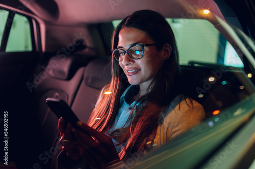 Business woman using smartphone while sitting in a backseat of a car at night photo