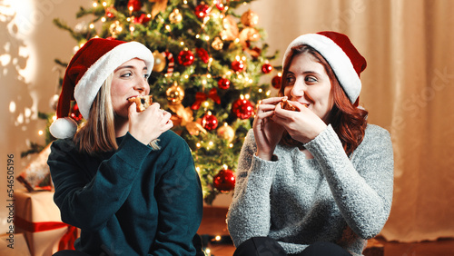 Two girls are eating the Christmas sweet Italian Panettone against the tree photo