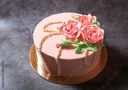 Beautiful pink cream cake decorated with beads and roses on a dark background