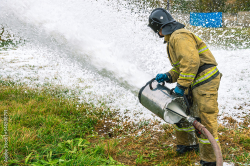 A firefighter in protective clothing extinguishes the fire by feeding foam. A firefighter extinguishes a fire with a foam generator. Extinguishing a fire in a tank farm with flammable liquids.