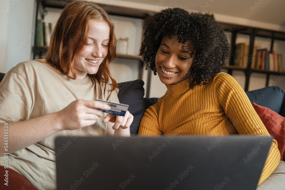 Couple of lesbian girlfriends buying online on e-commerce websites having fun together sitting on the sofa