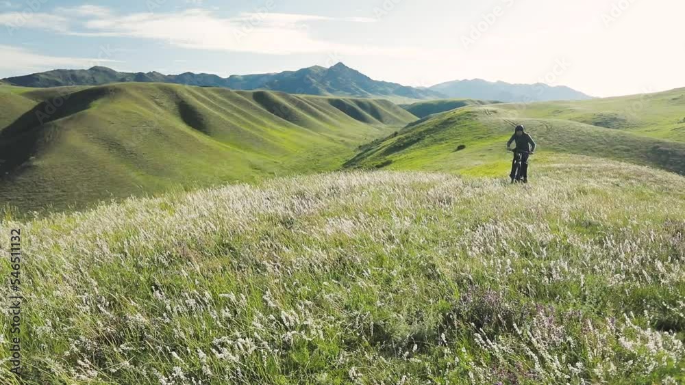 Man ride mountain bike at the green hill in the mountain of Kazakhstan Man ride mountain bike at the green hill in the mountain of Kazakhstan