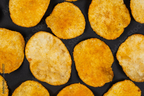 Delicious crispy potato chips with spices on a black background, top view