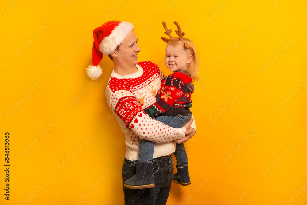 Happy smiling family father and daughter wearing Christmas sweaters, Santa Claus hat, reindeer antlers headwear and laughing on yellow background.
Young man and little girl celebrating New Year. Happy smiling family father and daughter wearing Christmas sweaters, Santa Claus hat, reindeer antlers headwear and laughing on yellow background.
Young man and little girl celebrating New Year.