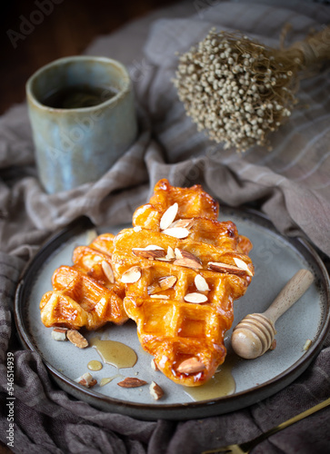 2 piece of croffles, almond and sweet syrup, honey,  serve in ceramic plate with a cup of tea on wood table, nature light, food issue, selective focus.