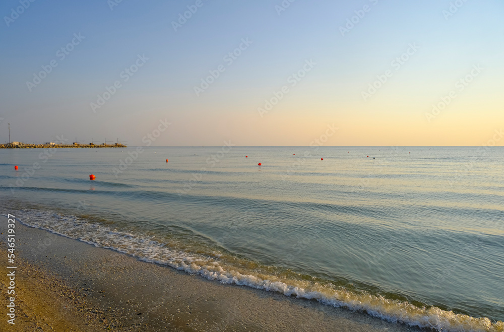 sunrise at the sandy beach with a line of red buoys. Coastline, horizontal line, natural background. Sun rising