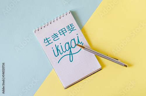 ikigai inscription in English and Chinese in a notebook on a yellow-blue background. ikigai - Japanese philosophy and life style - a reason for being 