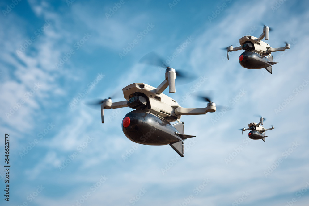 three consumer civilian drones with a big bomb on board flies in the blue  sky Photos | Adobe Stock