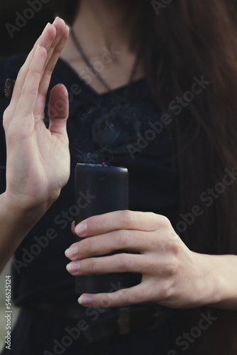 Close up extinct black candle concept photo. Withcy dressed woman. Front view photography with female hands on background. High quality picture for wallpaper, travel blog, magazine, article photo