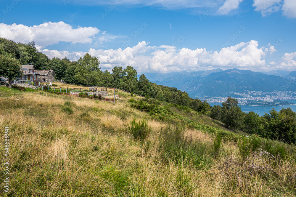 Mountain landscape with stone houses, blue sky and clouds with Lake Maggiore in the background