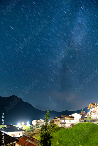 A small star trail with milky way visible above a small town in alps, Sauris, Italy