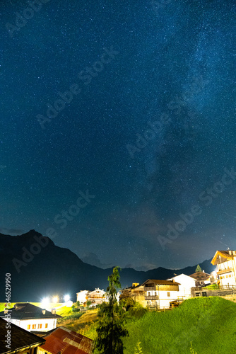Beautiful night sky with stars and milky way visible above a small village in alps, Sauris, Italy