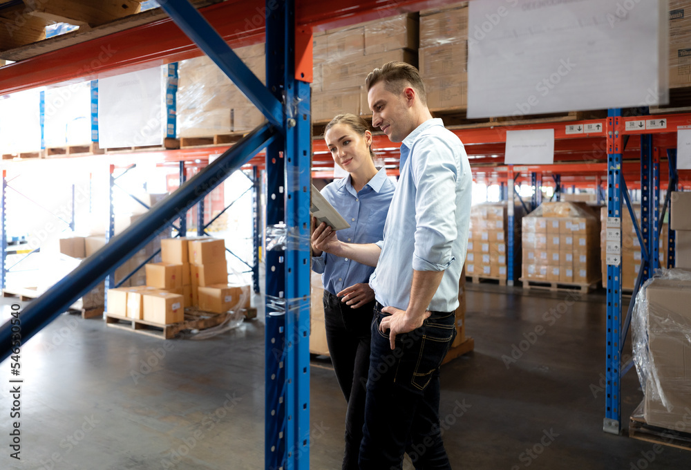 Distribution warehouse manager and client businesswoman using digital tablet checking inventory storage on shelf. Storehouse supervisor worker and logistic engineer standing together at storage room.