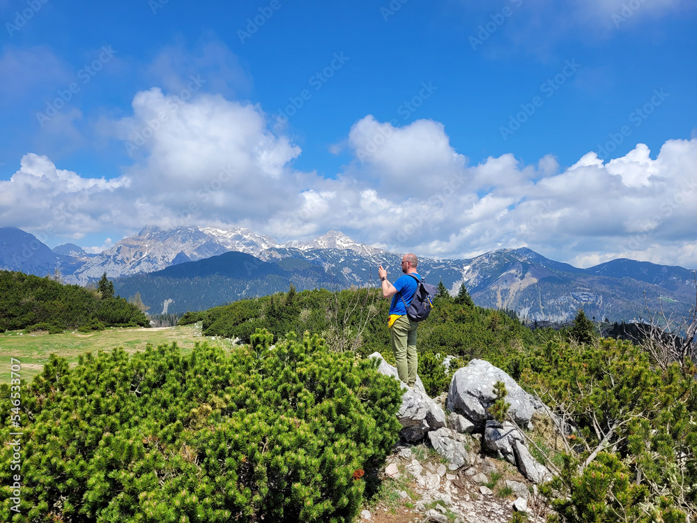 Happy man enjoys views of the alpine village in the mountains. Velika Planina or Big Pasture Plateau in the Kamnik Alps, Slovenia. Mountain cottage hut against blue sky