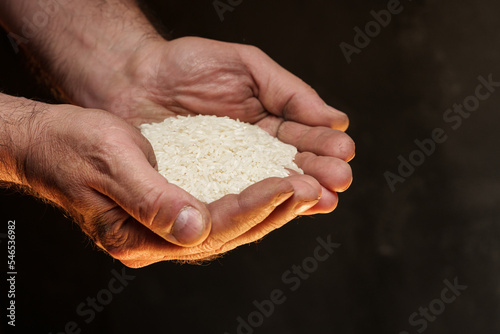 Hands holding a heap of dry rice grain on black background