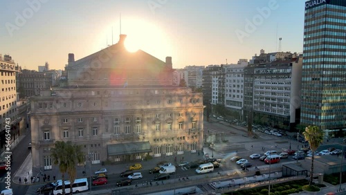 Aerial panning view capturing colon theater on the rear entrance, busy downtown rush hour traffics on 9 de julio avenue with big glowing sun in the background at sunset, Buenos Aires city, Argentina. photo