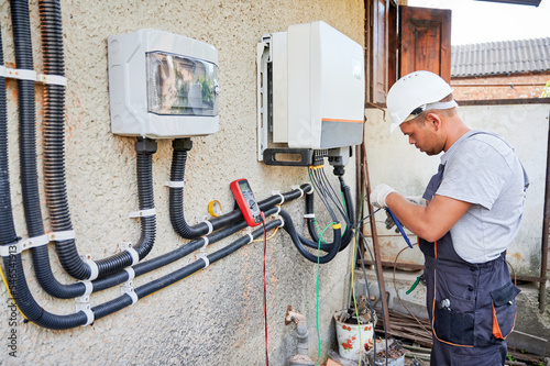 Man electrician installing solar panel system. Inspector in helmet and gloves making electrical wiring inverter and electric box. Concept of alternative and renewable energy. photo