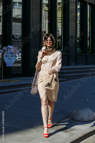A gorgeous girl in a dress and glasses walks around the city on a sunny day