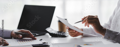 Young colleagues discuss business and analytical price charts using calculators and laptops to calculate financial, tax, accounting, statistics and analytical research ideas.