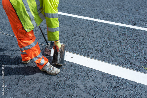 Road workers applying hot melt traffic resistant paint for white, yellow and red road marking lines on new build asphalt road