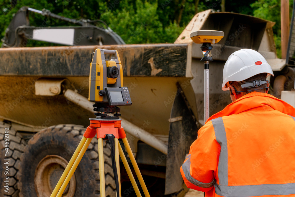 Surveyor site engineer with total positioning station on the construction site of the new road construction with construction machinery and materials  in the background