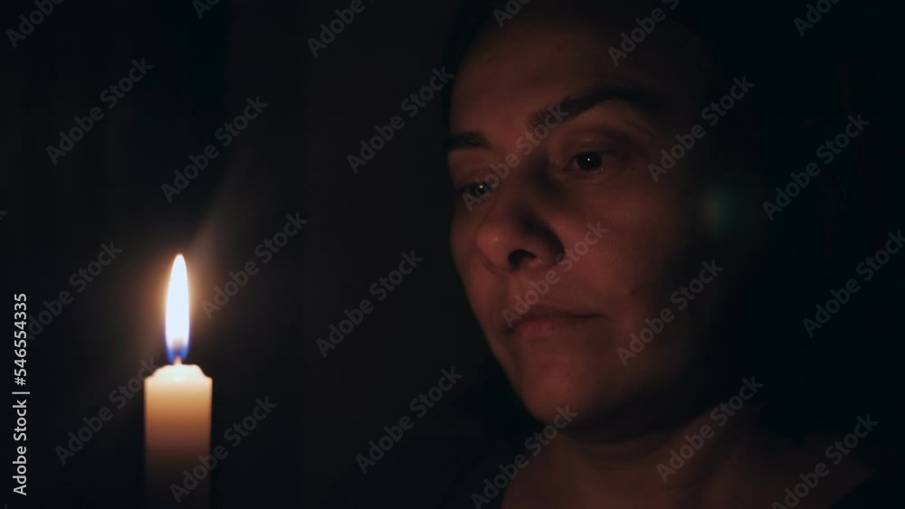 A Caucasian woman prays while standing in front of a burning candle. The girl gazes at the candle in front of her. A Caucasian woman prays while standing in front of a burning candle. The girl gazes at the candle in front of her.