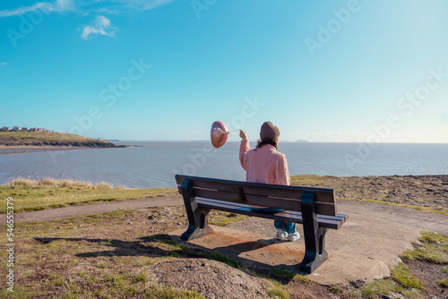 a young woman with baloon with heart in jeans and a pink jacket resting on the seashore