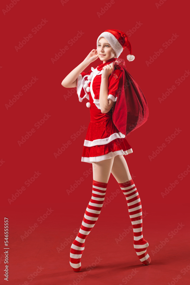 Dancing ballerina girl in pointe shoes with a gift in her hands dressed as Santa Claus on a red background. Dancing ballerina girl in pointe shoes with a gift in her hands dressed as Santa Claus on a red background.