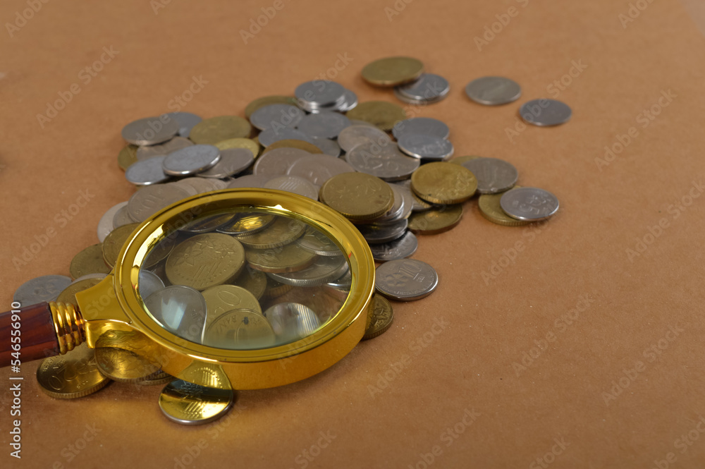 Pile of coins and magnifying glass. Finance, economy, stock market, saving and inflation concept