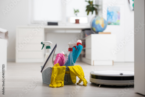 Picture of an automatic intelligent robotic vacuum cleaner and colorful cleaning product on the floor.