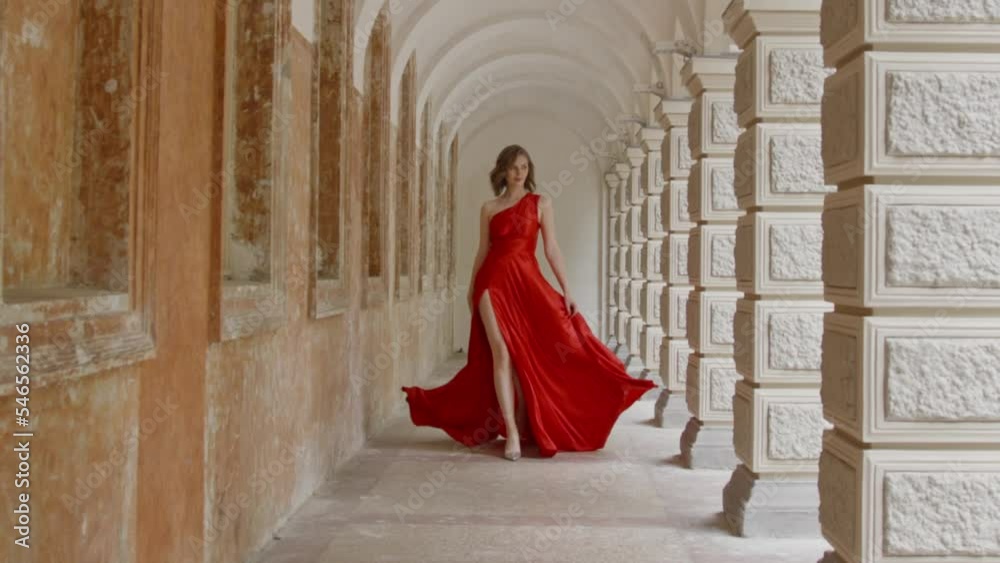 A beautiful blonde woman walks elegantly in a graceful red dress.
