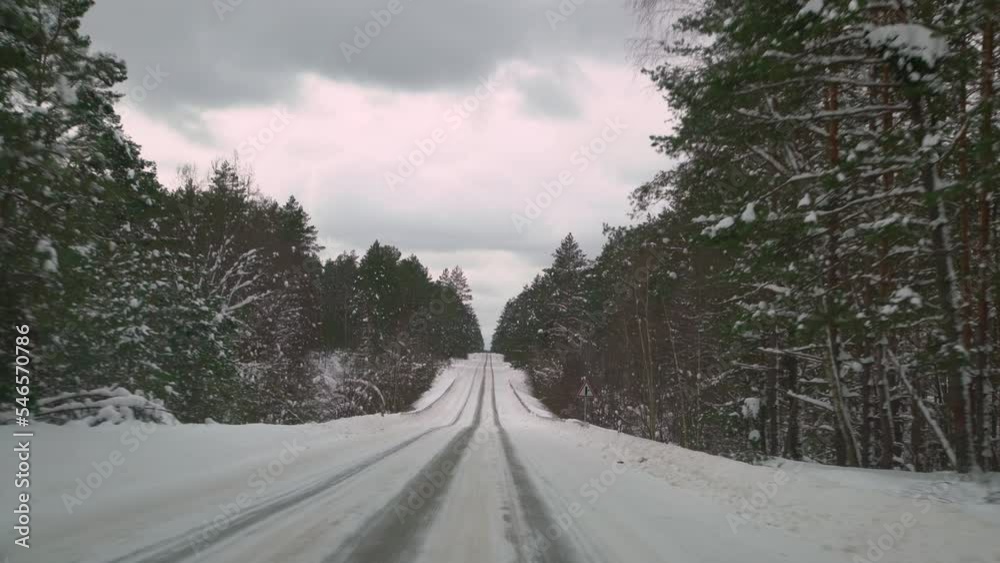 Driving with caution on a slippery road covered with snow in the forest. Car driving on empty path in winter.