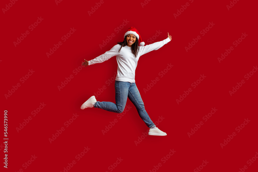 Emotional pretty black woman wearing Santa hat jumping over red