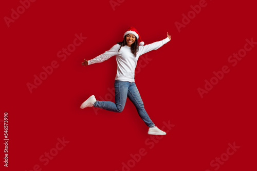 Emotional pretty black woman wearing Santa hat jumping over red