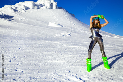 Sexy woman in silver cosmic outfit silver and winter boots is posing in the mountains. Female model in glamour silver jumpsuit in winter scenery. photo