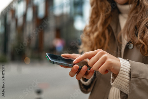 Curly woman wearing warm coat walking down the street and using her phone