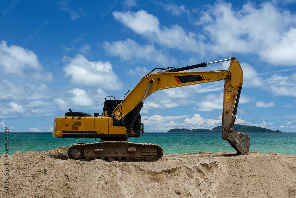 Excavator is scooping up sand on the beach with sky, sea and island background..Excavator is digging sand on the beach. Excavator is scooping up sand on the beach with sky, sea and island background..Excavator is digging sand on the beach.