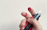 There is a red bloody wound on the finger, an accidental knife or cutter cut on the finger of a man or a woman.