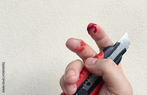There is a red bloody wound on the finger, an accidental knife or cutter cut on the finger of a man or a woman. © WIROT