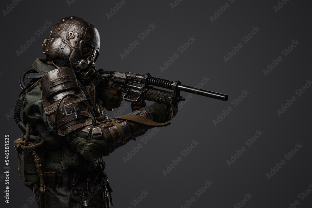 Portrait of military man in post apocalypse style dressed in armored suit aiming shotgun.