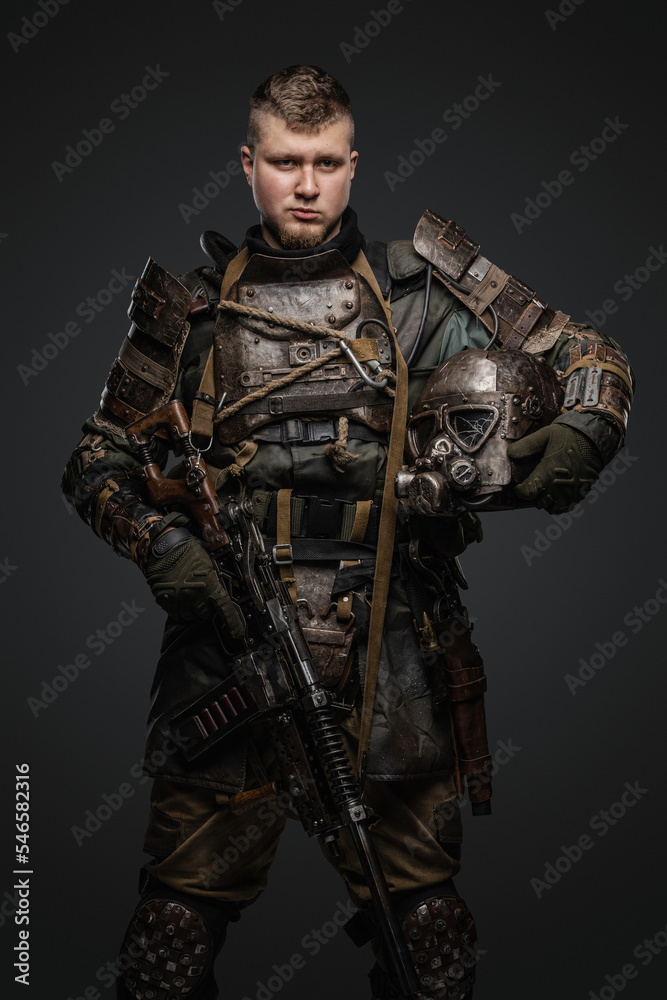 Shot of male survivor dressed in armor holding shotgun and helmet.